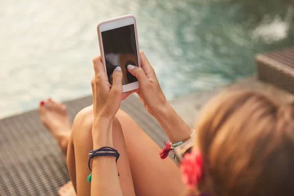 Chica usando el teléfono celular mientras está acostado en un salón de cubierta de piscina — Foto de Stock