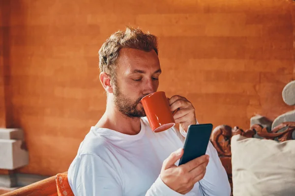 Hombre sentado en un sofá terraza y beber café / té mientras usa — Foto de Stock