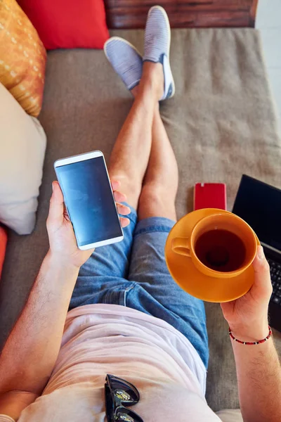 コーヒー/紅茶を飲みながら携帯電話とノートパソコンを使う男性 — ストック写真