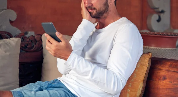 Hombre usando el teléfono celular mientras sititng en un sofá / sofá . — Foto de Stock