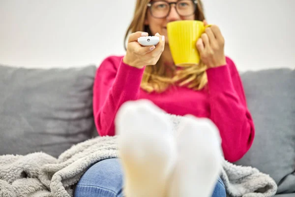 Dívka drží Tv remote a pití kávy / čaje na gauči. — Stock fotografie