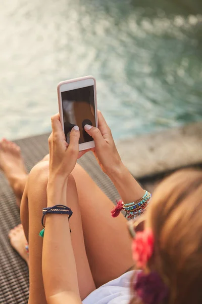 Chica usando el teléfono celular mientras está acostado en un salón de cubierta de piscina — Foto de Stock