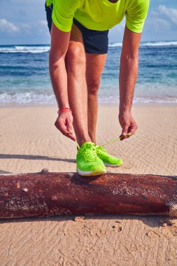 Bir tropikal egzotik plajda çalışan Sneakers bağlama adam.