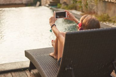 Bir yüzme havuzu güverte salonda yatarken cep telefonu kullanarak kız 