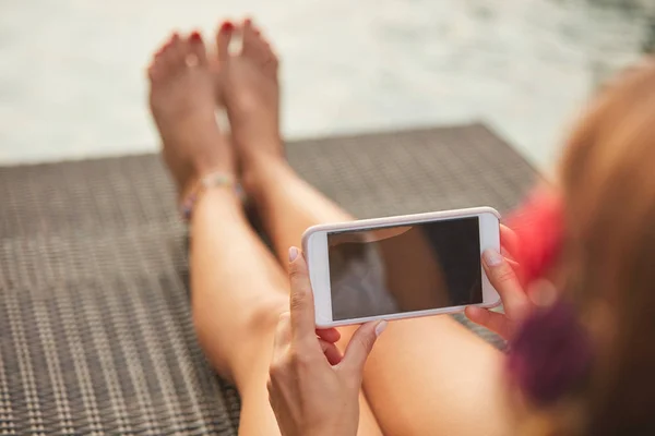 Meisje met behulp van mobiele telefoon liggend op een zwembad dek Lounge — Stockfoto