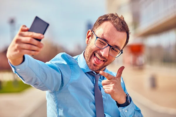 Divertido hombre de negocios con pulgares hacia arriba mientras usa el teléfono inteligente al aire libre —  Fotos de Stock
