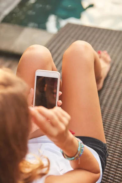 Дівчина використовує мобільний телефон, лежачи на вітальні басейну — стокове фото