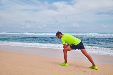 Sportsman stretching on a exotic tropical beach after jogging / 