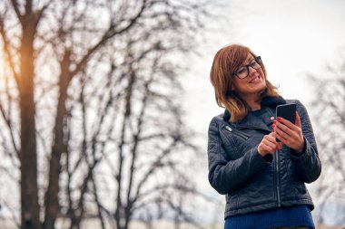 Sevimli genç kadın kullanarak Cellphone açık havada.