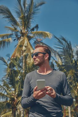 Cep telefonu kullanan adam / smartphone tropikal ortamda.