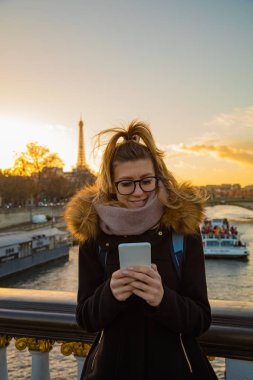 Paris geçmişi ve Eyfel kulesi olan cep telefonu kullanan bir kız.