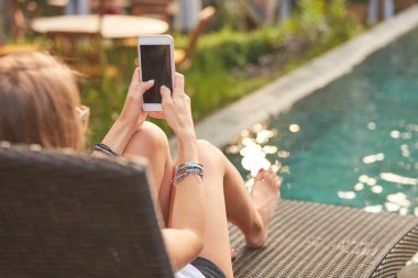 Bir yüzme havuzu güverte salonda yatarken cep telefonu kullanarak kız 