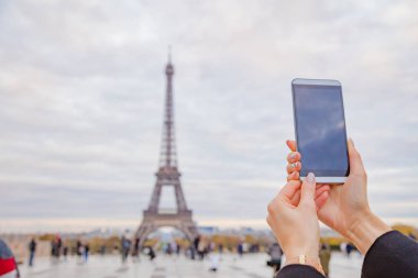 Paris geçmişi ve Eyfel kulesi olan cep telefonu kullanan bir kız.