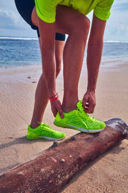 Bir tropikal egzotik plajda çalışan Sneakers bağlama adam.