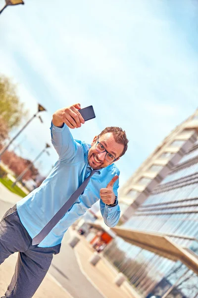 Divertido hombre de negocios con pulgares hacia arriba mientras usa el teléfono inteligente al aire libre —  Fotos de Stock