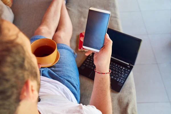 Muž používající mobilní telefon a laptop při pití kávy/čaje na Th — Stock fotografie