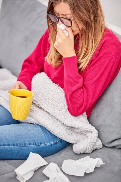 Niña enferma sosteniendo la taza y bebiendo café / té en un sofá . —  Fotos de Stock