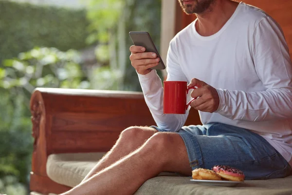 Hombre sentado en un sofá terraza y beber café / té, comer hacer — Foto de Stock