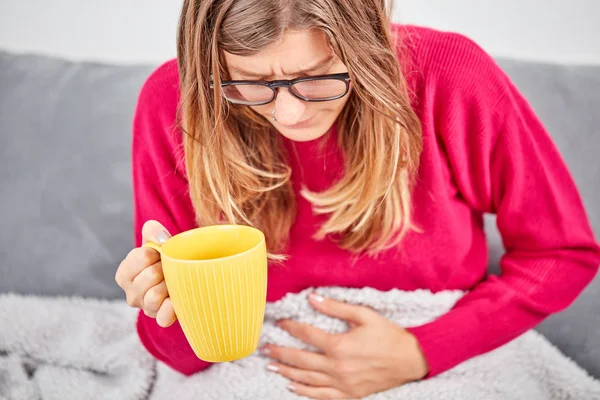 Niña enferma sosteniendo la taza y bebiendo café / té en un sofá . —  Fotos de Stock