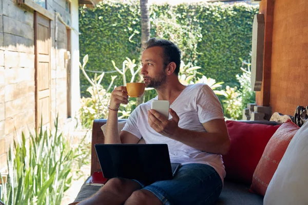 Hombre usando el teléfono celular y el ordenador portátil mientras bebe café / té en th — Foto de Stock