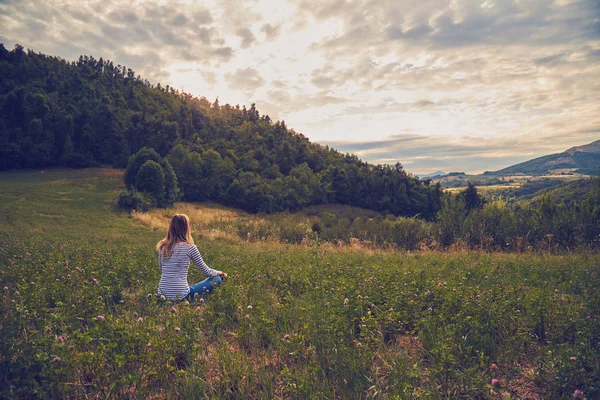 Κορίτσι κάθεται σε ένα καταπράσινο λιβάδι και βλέποντας την ύπαιθρο γη — Φωτογραφία Αρχείου