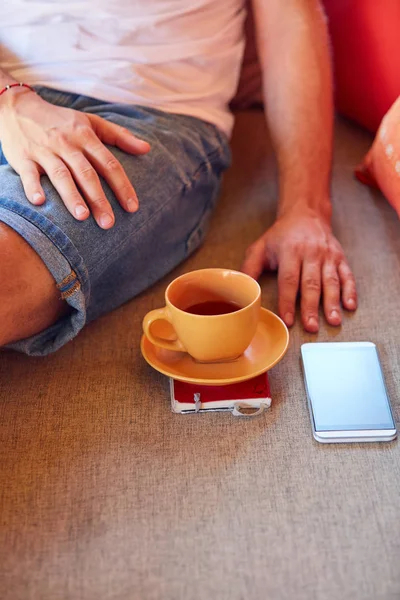 Man met behulp van mobiele telefoon tijdens het drinken van koffie/thee op de Bank. — Stockfoto