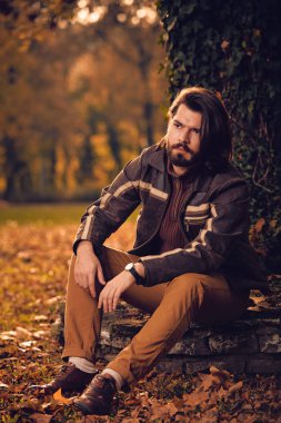Sonbahar renkli parkta ağacın yanında oturan adam.