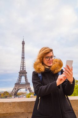Paris geçmişi ve Eyfel kulesi olan cep telefonu kullanan bir kız.