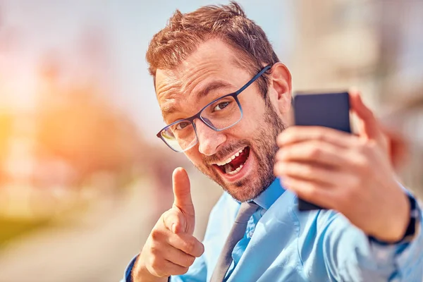 Divertido hombre de negocios con pulgares hacia arriba mientras usa el teléfono inteligente al aire libre —  Fotos de Stock