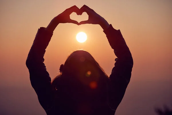 Menina fazendo coração - sinal de forma com as mãos ao pôr do sol / nascer do sol ti — Fotografia de Stock