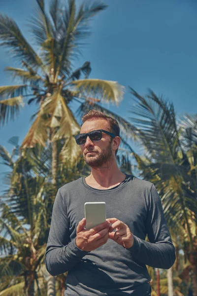 Hombre usando teléfono celular / smartphone en ambiente tropical . —  Fotos de Stock