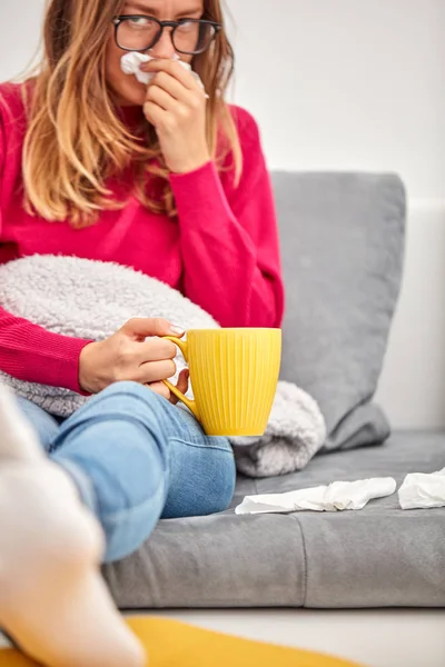 Niña enferma sosteniendo la taza y bebiendo café / té en un sofá . —  Fotos de Stock