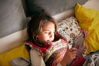 Küçük kız okuyor ve tablet ile evde ödev yapıyor.