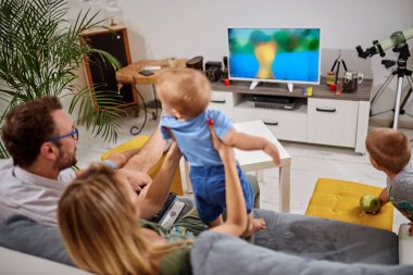 Genç ebeveynler, Bebek çocuklarla TV izliyor.