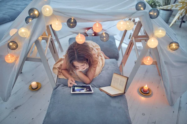 Piccola bambina di 10 anni utilizzando tablet sotto la sua tenda fatta in casa in — Foto Stock