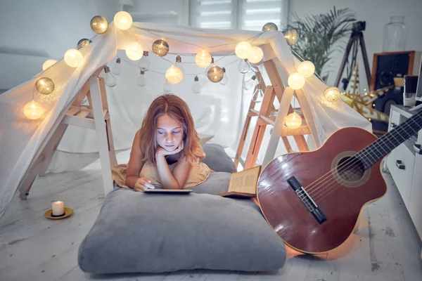 Pequeña niña de 10 años usando tableta debajo de su tienda de campaña casera en — Foto de Stock