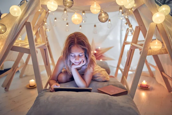 Piccola bambina di 10 anni utilizzando tablet sotto la sua tenda fatta in casa in — Foto Stock