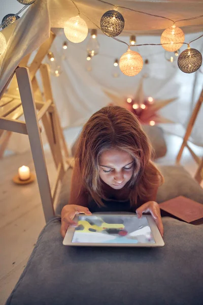 Piccola bambina di 10 anni utilizzando tablet sotto la sua tenda fatta in casa in — Foto Stock