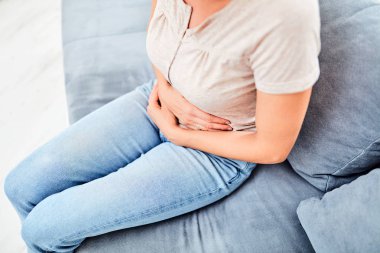 Woman with  stomach issues / problems while sitting on the couch clipart