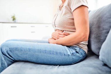 Kanepede otururken mide sorunları olan bir kadın.