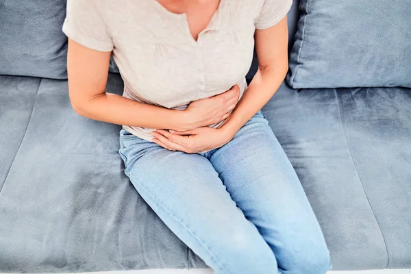 Mujer con problemas de estómago / problemas mientras está sentada en el sofá —  Fotos de Stock