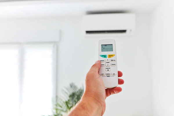 Modern air conditioner unit with a hand holding a remote.