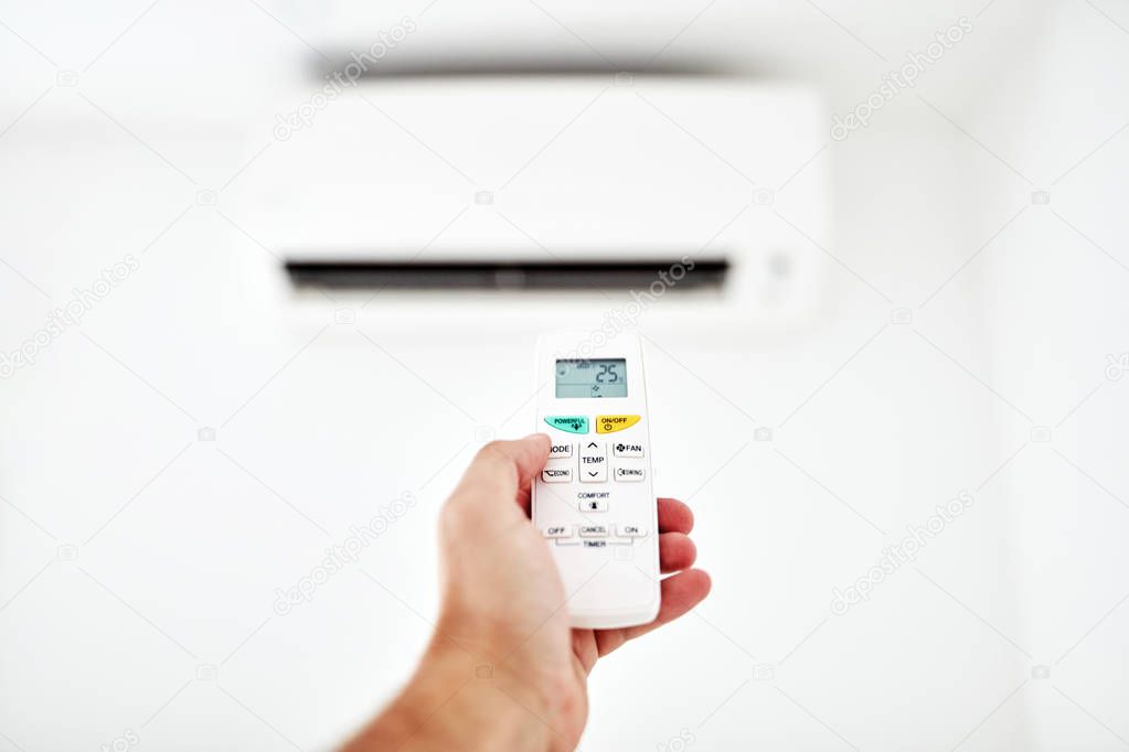 Modern air conditioner unit with a hand holding a remote.