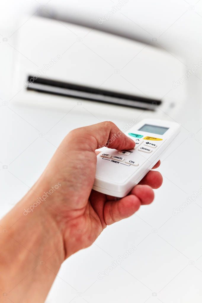 Modern air conditioner unit with a hand holding a remote.