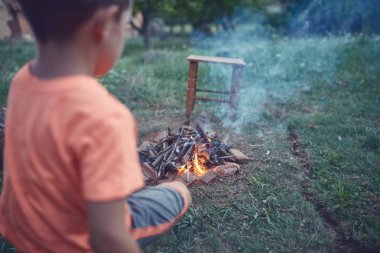 Küçük çocuk çayırda kamp ateşi yakıyor..