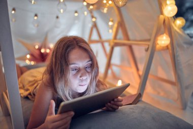 Ev yapımı çadırının altında tablet kullanan 10 yaşında bir kız.