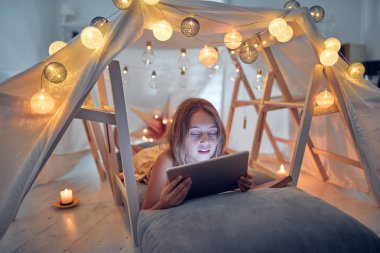 Ev yapımı çadırının altında tablet kullanan 10 yaşında bir kız.