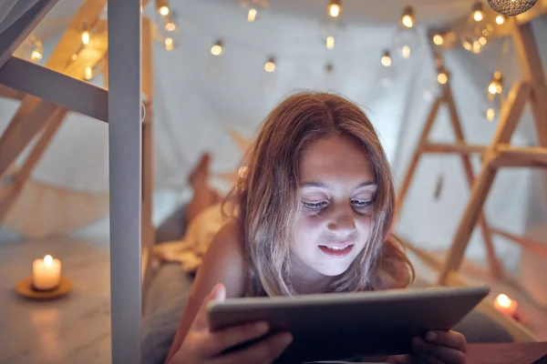 Piccola bambina di 10 anni utilizzando tablet sotto la sua tenda fatta in casa in — Foto Stock