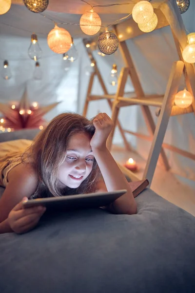 Piccola bambina di 10 anni utilizzando tablet sotto la sua tenda fatta in casa in — Foto Stock