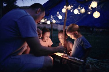 Baba ve çocuklar arka bahçedeki çadırın altında oynuyorlar..
